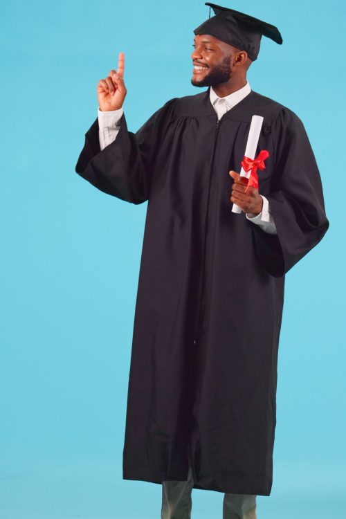 Black man, graduation and point up for education achievement, university advertising and diploma on blue background. Success, future and certified, academic course promotion and graduate in studio.